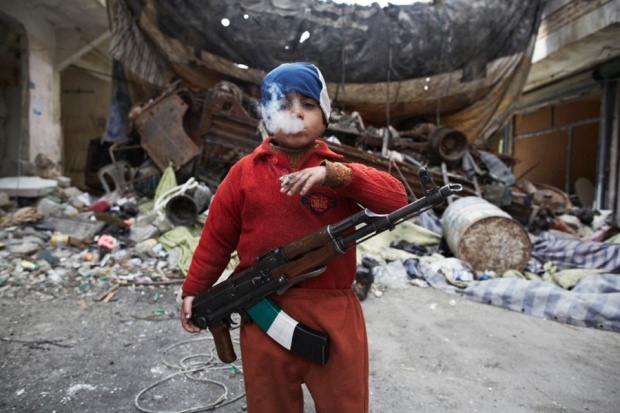 8-year-old Ahmed, a Syrian child soldier, smokes while holding his AK47. Source: Sebastiano Tomada Piccolomini.